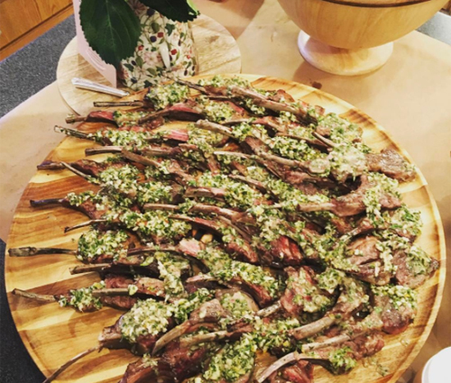 A large number of baby lamb chops arranged on a round wooden platter